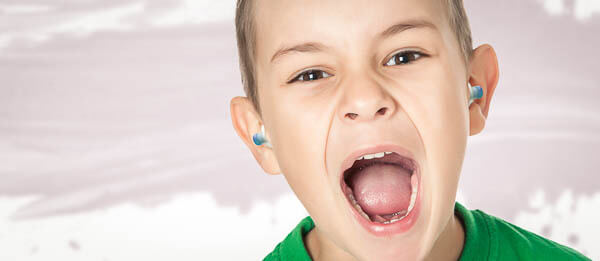 Kind schreit mit Ohrstöpseln im Ohr.