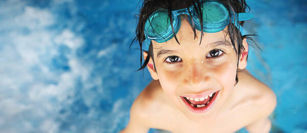Ein Junge im Schwimmbad mit Ohrstöpseln im Ohr und Taucherbrille auf dem Kopf.
