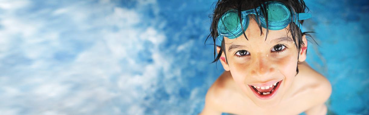 Junge spielt im Schwimmbad mit Taucherbrille und Ohrstöpseln.