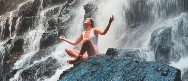 Eine Frau meditiert in Ruhe an einem lauten Wasserfall