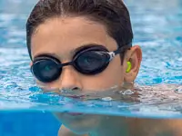 Junge im Wasser mit SNUGOS Silikonstöpsel im Ohr.