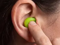 Nahaufnahme eines Fingers, der einen grünen, formbaren Snugos Ohrstöpsel sanft in die äußere Ohrmuschel drückt und anpasst.