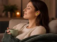 Eine entspannte Frau sitzt mit geschlossenen Augen und einer Tasse auf dem Sofa, geschützt durch grüne Snugos Ohrstöpsel vor Umgebungslärm.
