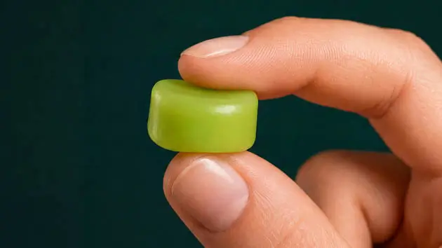 Nahaufnahme von Daumen und Zeigefinger, die einen einzelnen, grünen Snugos Silikon-Ohrstöpsel halten und seine weiche, zylinderförmige Beschaffenheit zeigen.
