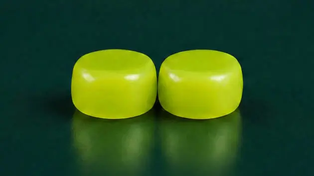 Zwei leuchtend grüne, formbare Snugos Silikon-Ohrstöpsel liegen nebeneinander auf einer dunklen Oberfläche.
