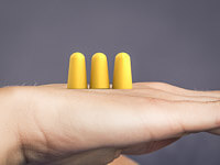 Drei gelbe Ohrstöpsel stehen auf einer Handfläche.