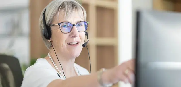 Eine Frau mit einem Headset zeigt auf einen Monitor