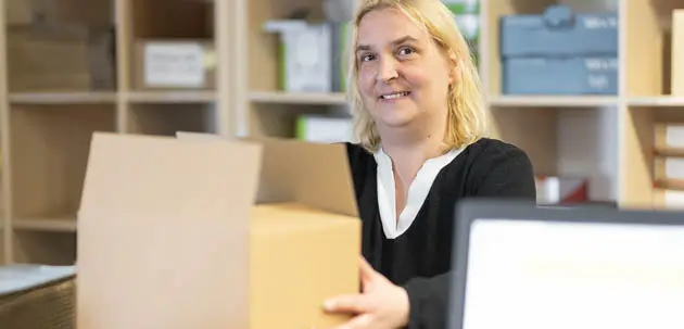 Eine Frau lächelt und hält einen Karton in der Hand